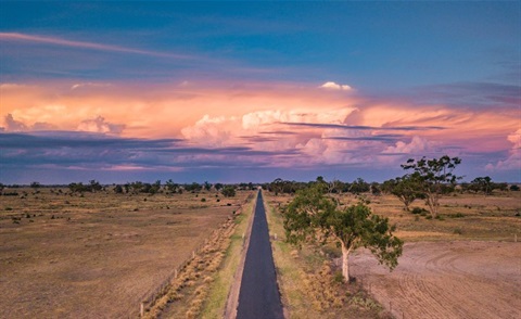 drone shot of road leading into the horizon with a pink sunset and storm clouds